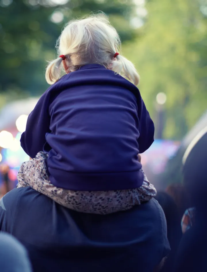 Une petite fille sur les épaules d’un adulte lors d’un événement en plein air