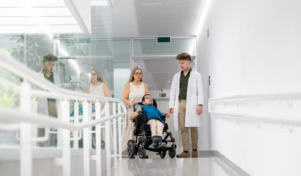 Une soignante accompagne un homme en fauteuil roulant dans un couloir d’hôpital